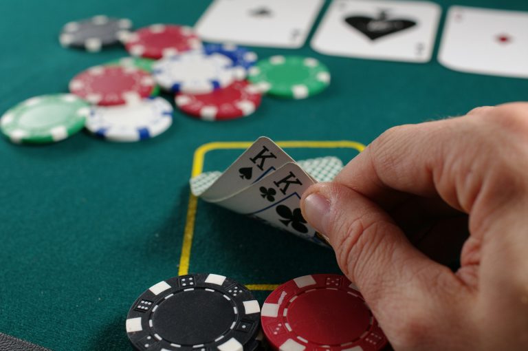 Poker game showing a player's hand holding two King cards. Stacks of poker chips in various colors, including black, blue, white, and green, are arranged on the green felt table
